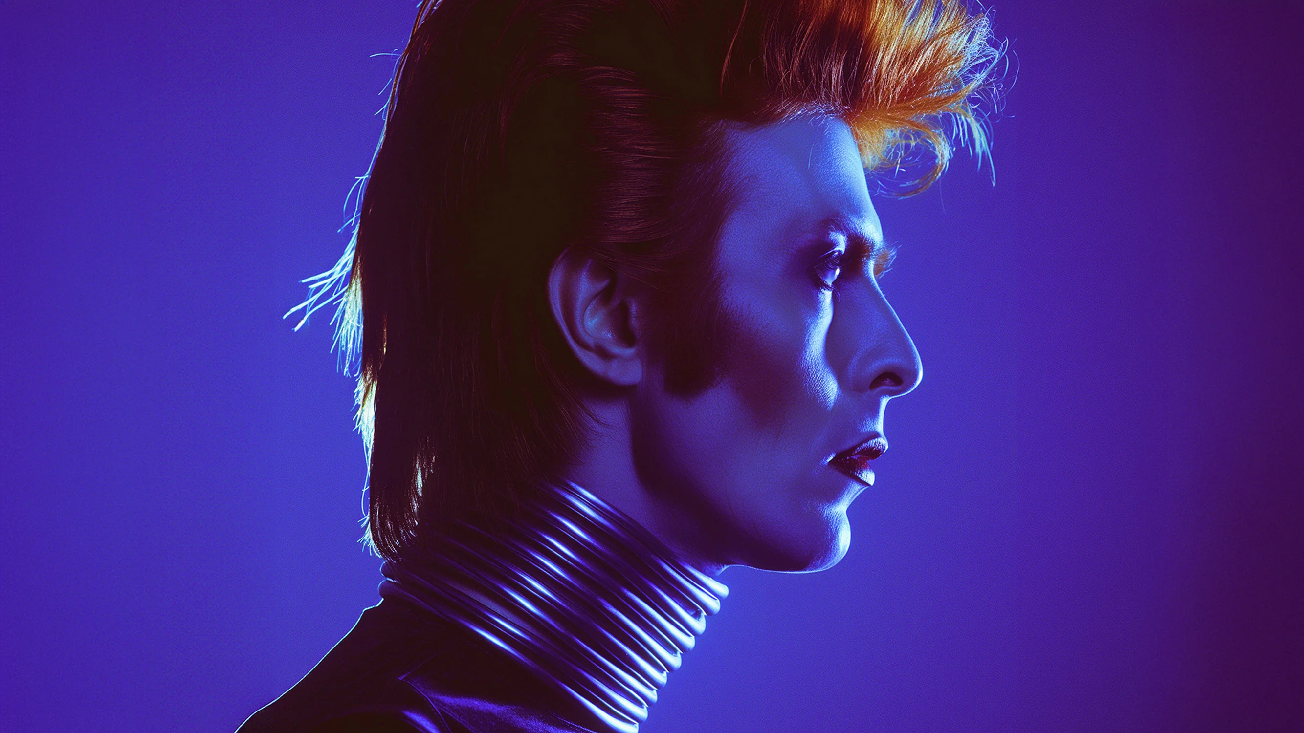 Side profile of a person with bright orange styled hair, dramatic makeup, and a shiny metallic coil neckpiece against a purple background.