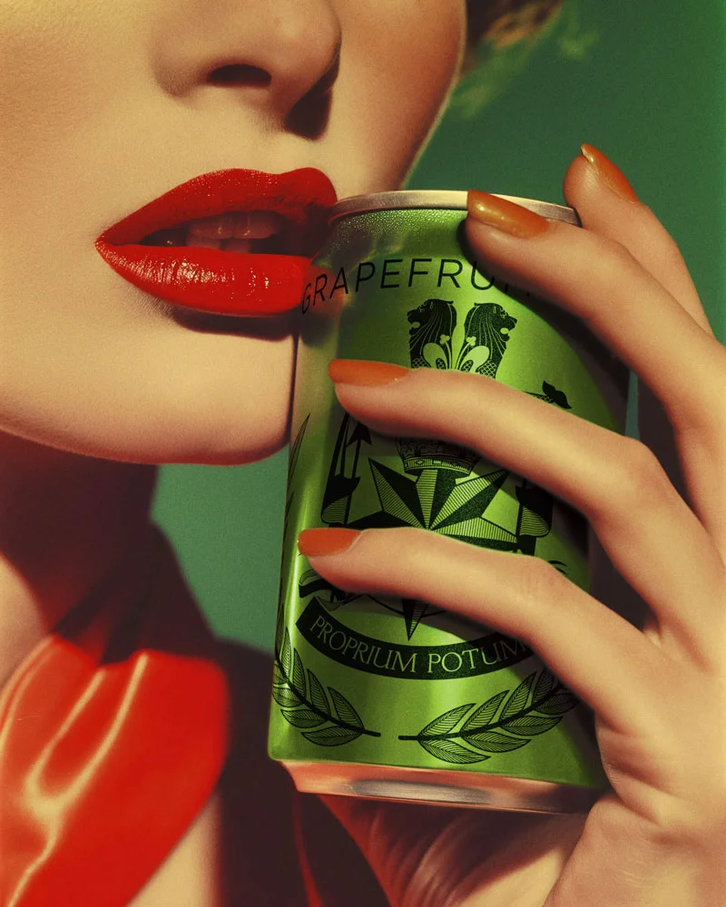 Close-up of a person with bright red lipstick and orange nail polish holding a green grapefruit soda can near their lips.