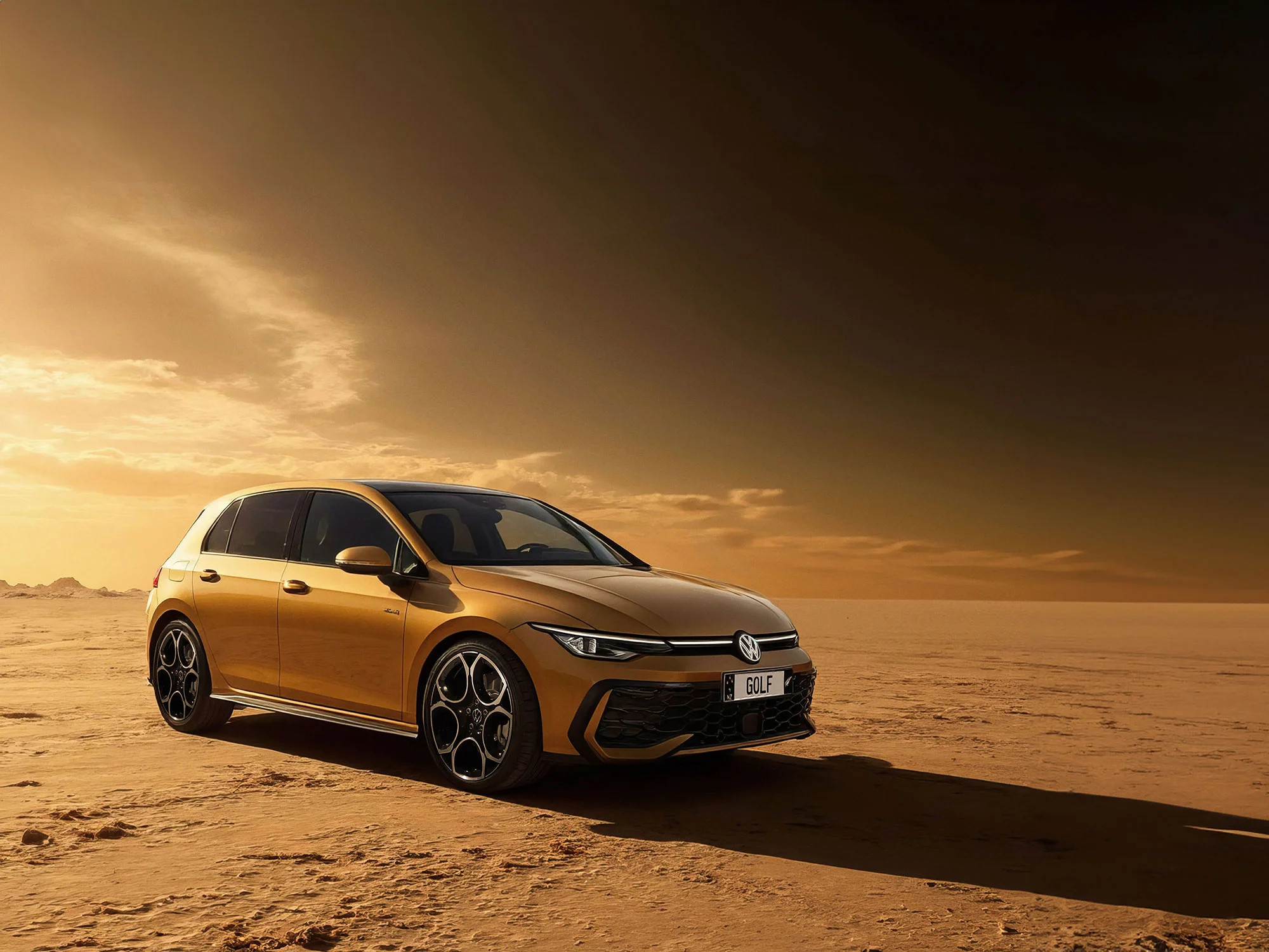Golden Volkswagen Golf hatchback parked on a desert landscape with dramatic sunset sky.