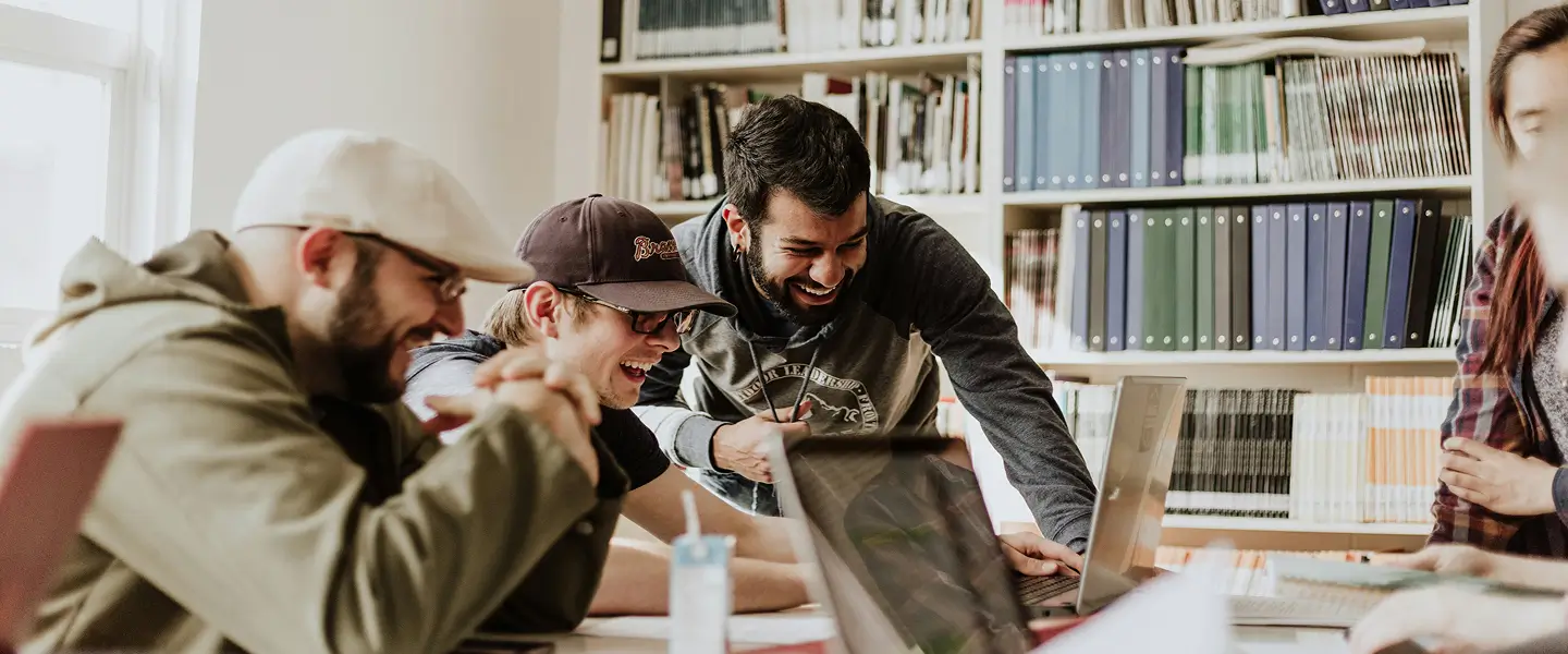 A group of students sitting around a laptop laughing.