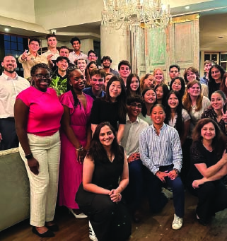 Diverse group of young adults posing indoors in front of a vintage cabinet and chandelier.