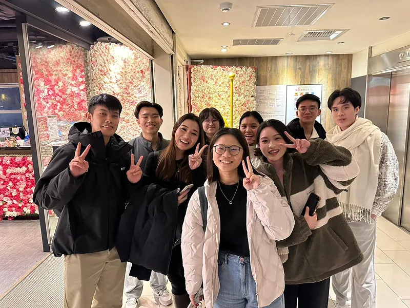 Six people wearing straw hats stand in a green field with mountains in the background.