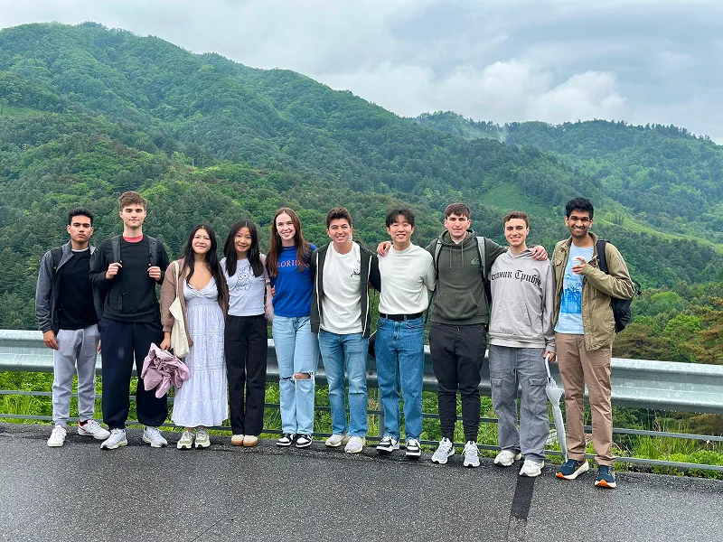 Group of diverse young adults jumping cheerfully on a tree-lined path outdoors.