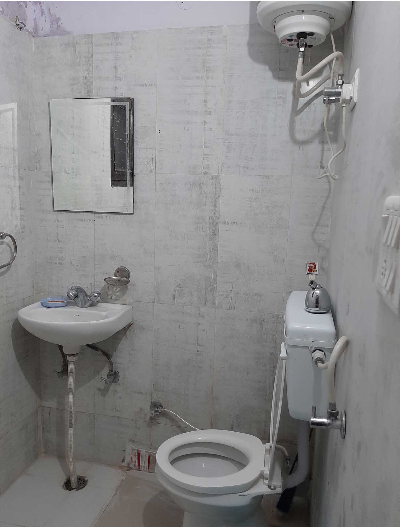  A compact bathroom with a small sink, a mirror, and a water heater mounted on the wall. The room is tiled in white.
