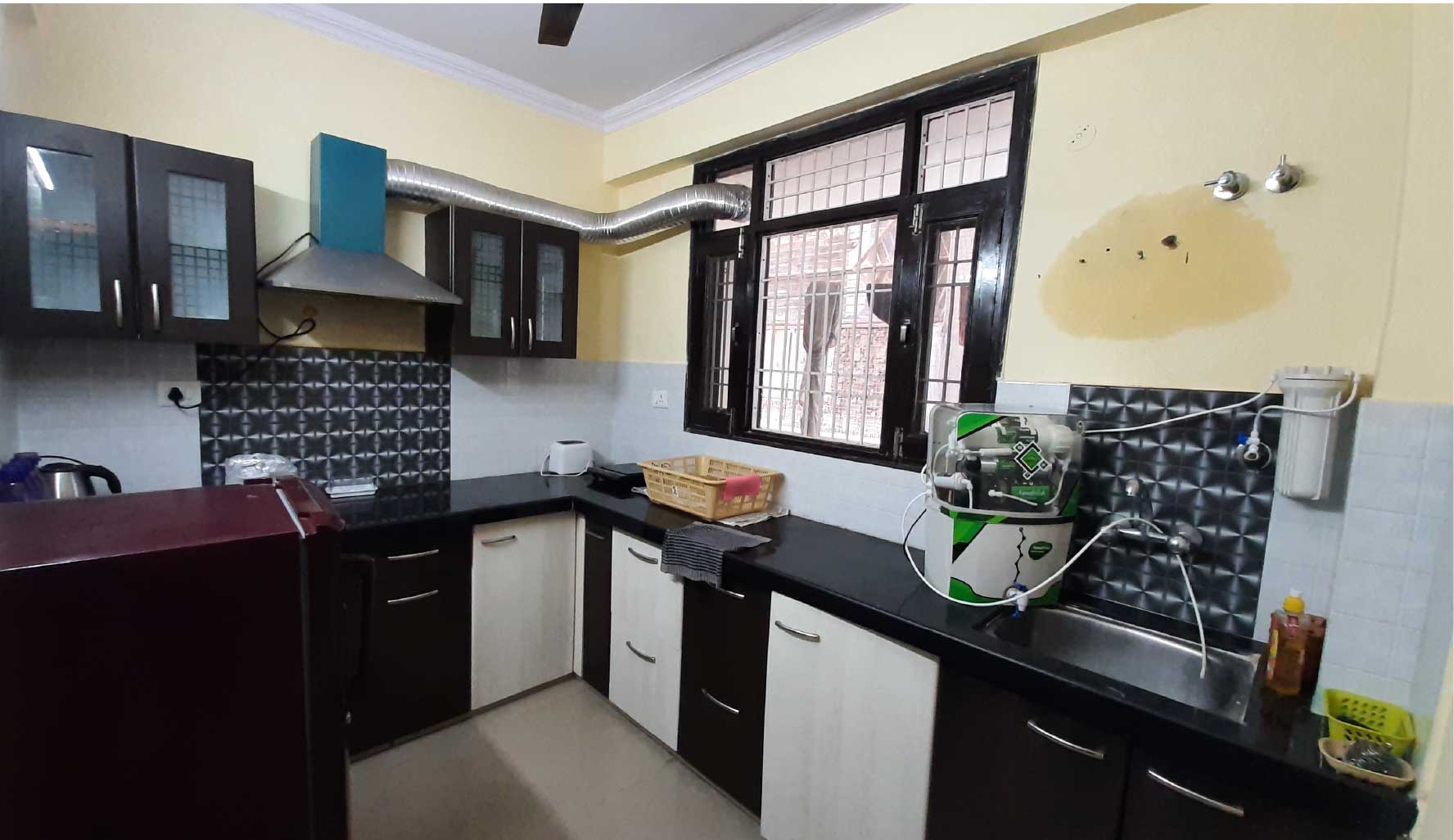 A kitchen featuring wooden cabinets, a tiled backsplash, and black countertops. Large windows provide natural light.