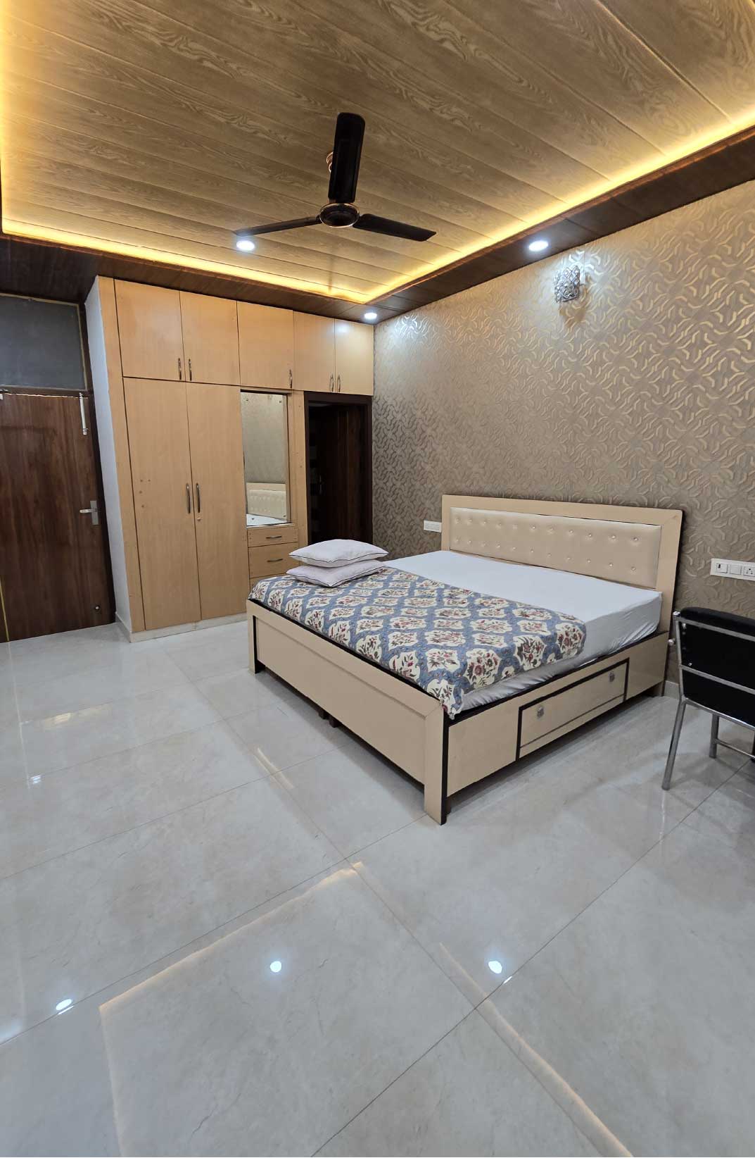 A cozy bedroom with a double bed, wooden furniture, and neutral-colored walls. The room has bright lighting and modern furnishings.