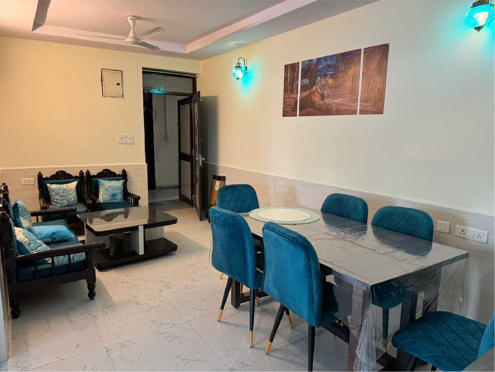 A dining area with a rectangular table, teal chairs, and wall art. The room has bright lighting and a polished floor.