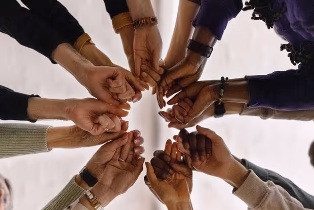 Verschiedene Hände verschiedener Hautfarben bilden einen Kreis und berühren sich mit den Fingerspitzen.