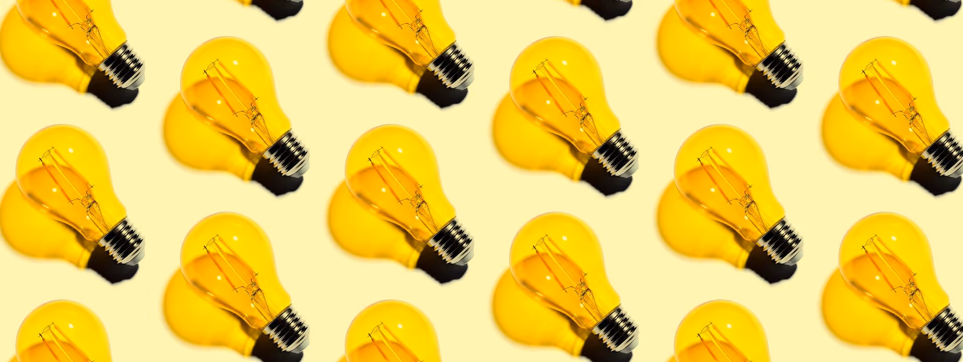 Mehrere gelbe Glühbirnen mit sichtbaren Filamenten auf hellem Hintergrund angeordnet.
