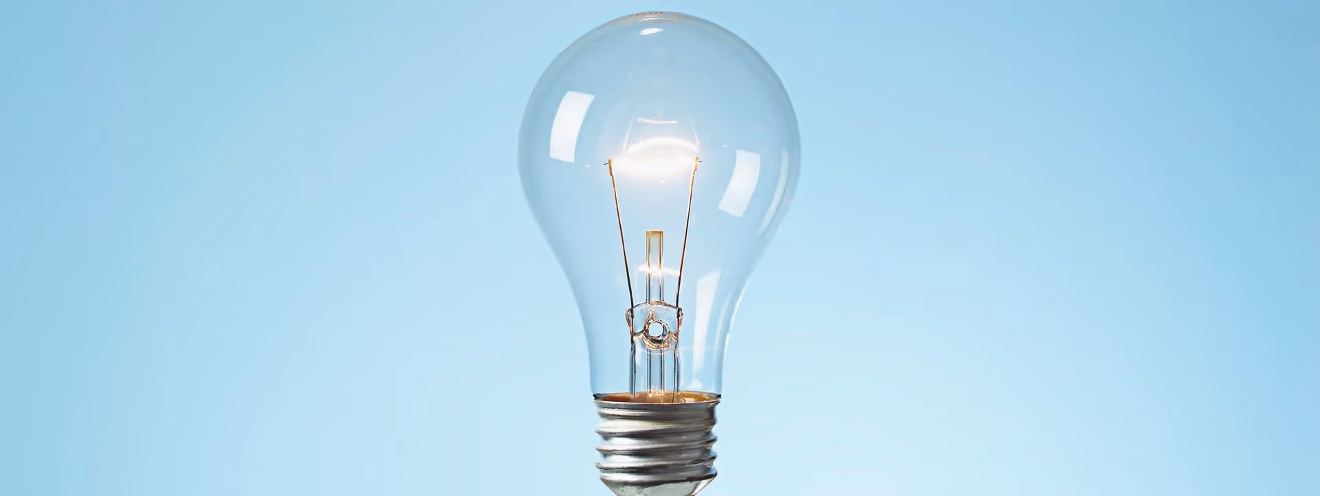 Glühbirne mit anliegender glühender Glühbirnenwendel vor blauem Hintergrund.