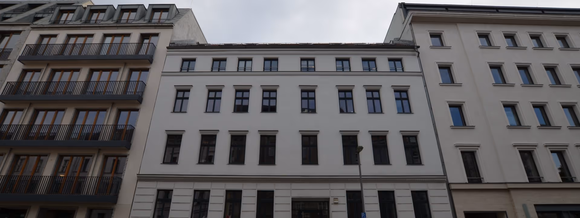 Fassade eines mehrstöckigen Gebäudes mit mehreren Fenstern unter einem bewölkten Himmel.