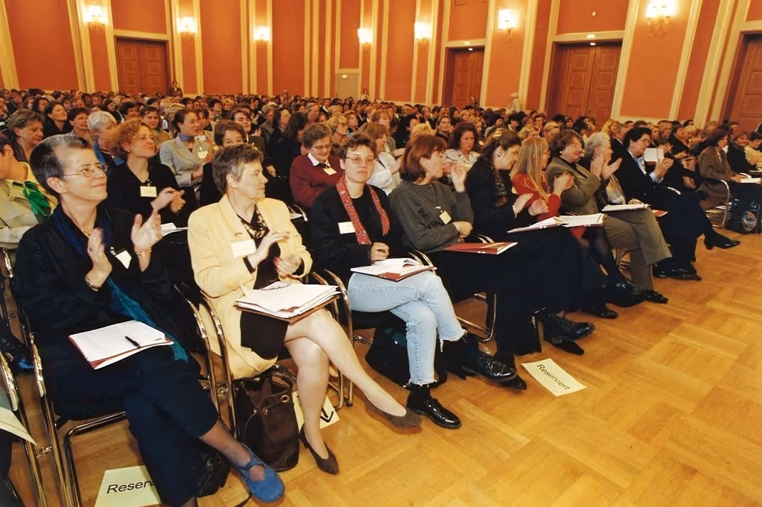 Große Gruppe von Frauen, die in einem Saal auf Stühlen sitzen und applaudieren.