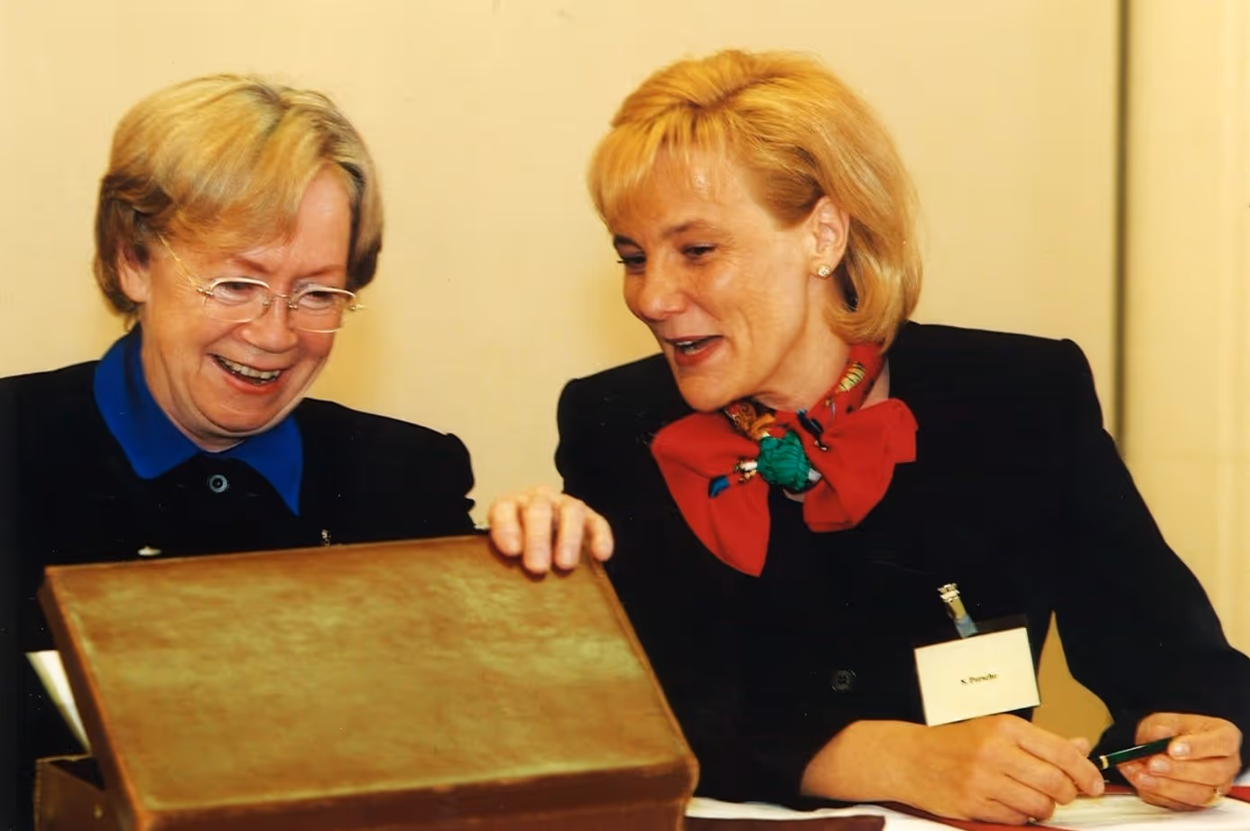 Zwei Frauen lachen und schauen gemeinsam in einen geöffneten braunen Koffer.