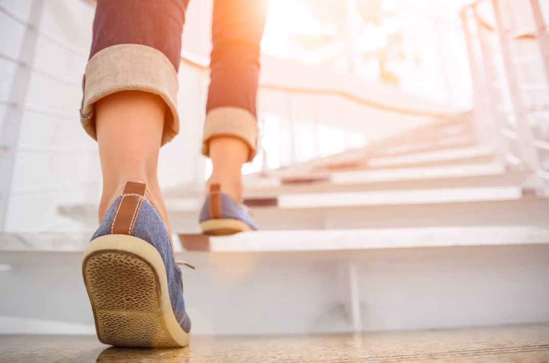 Person geht in blauen Turnschuhen eine helle Treppe hinauf mit hochgekrempelten Hosenbeinen.