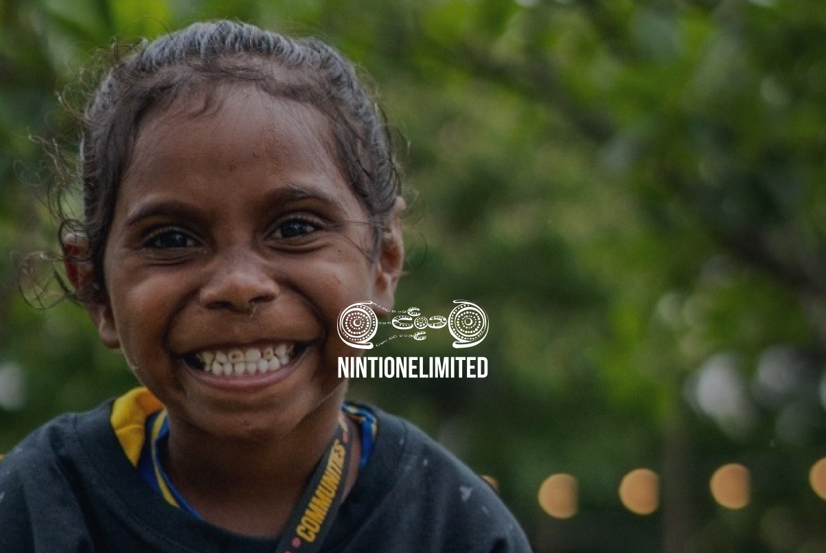 Smiling young child outdoors with blurred green trees in the background.