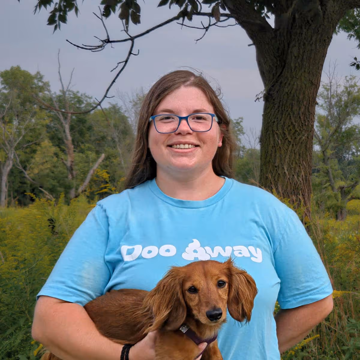 portrait of Alyssa in blue Doo Away shirt holding her brown Dachshund dog Luna