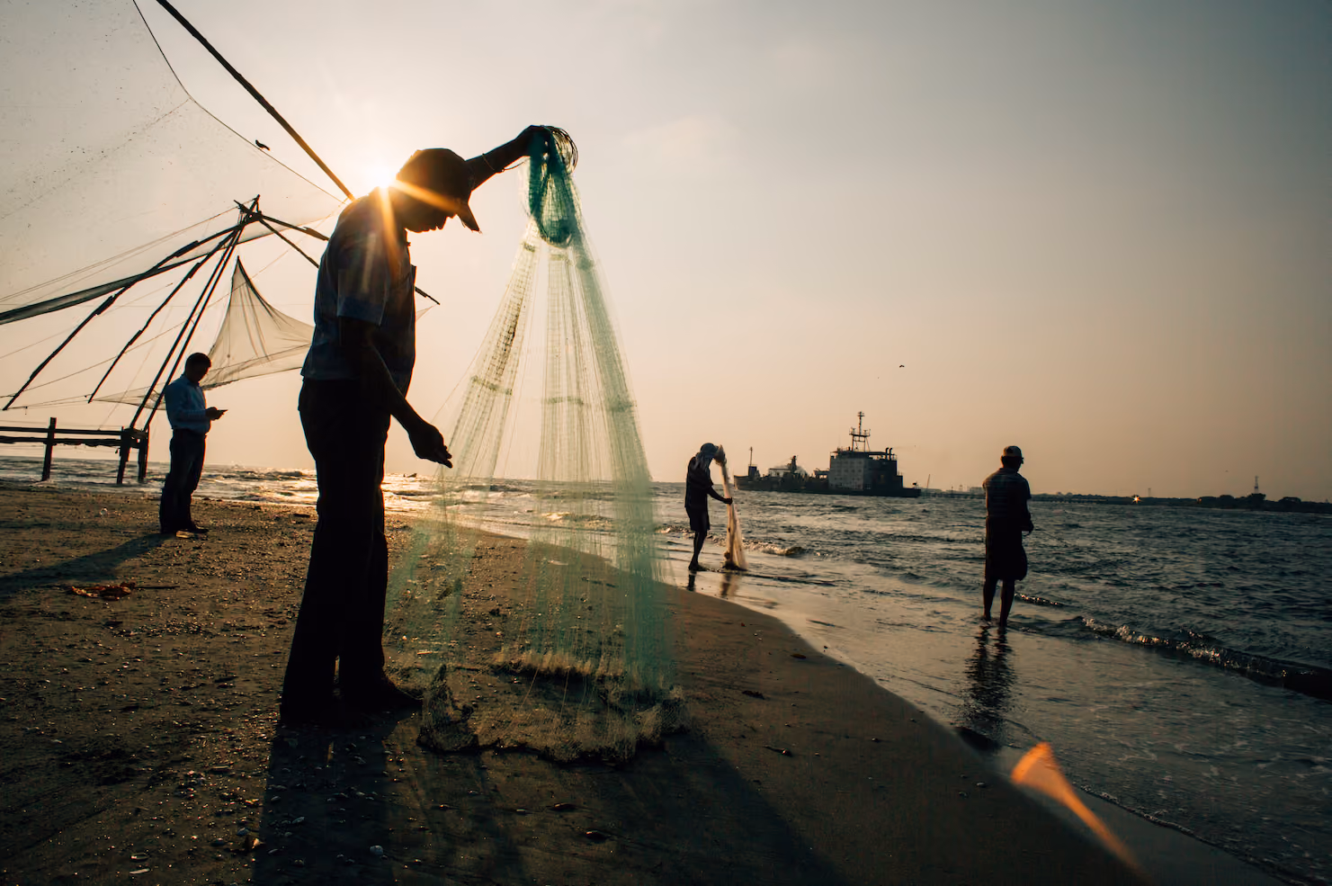 Fishermen hauling nets on a beach at sunset