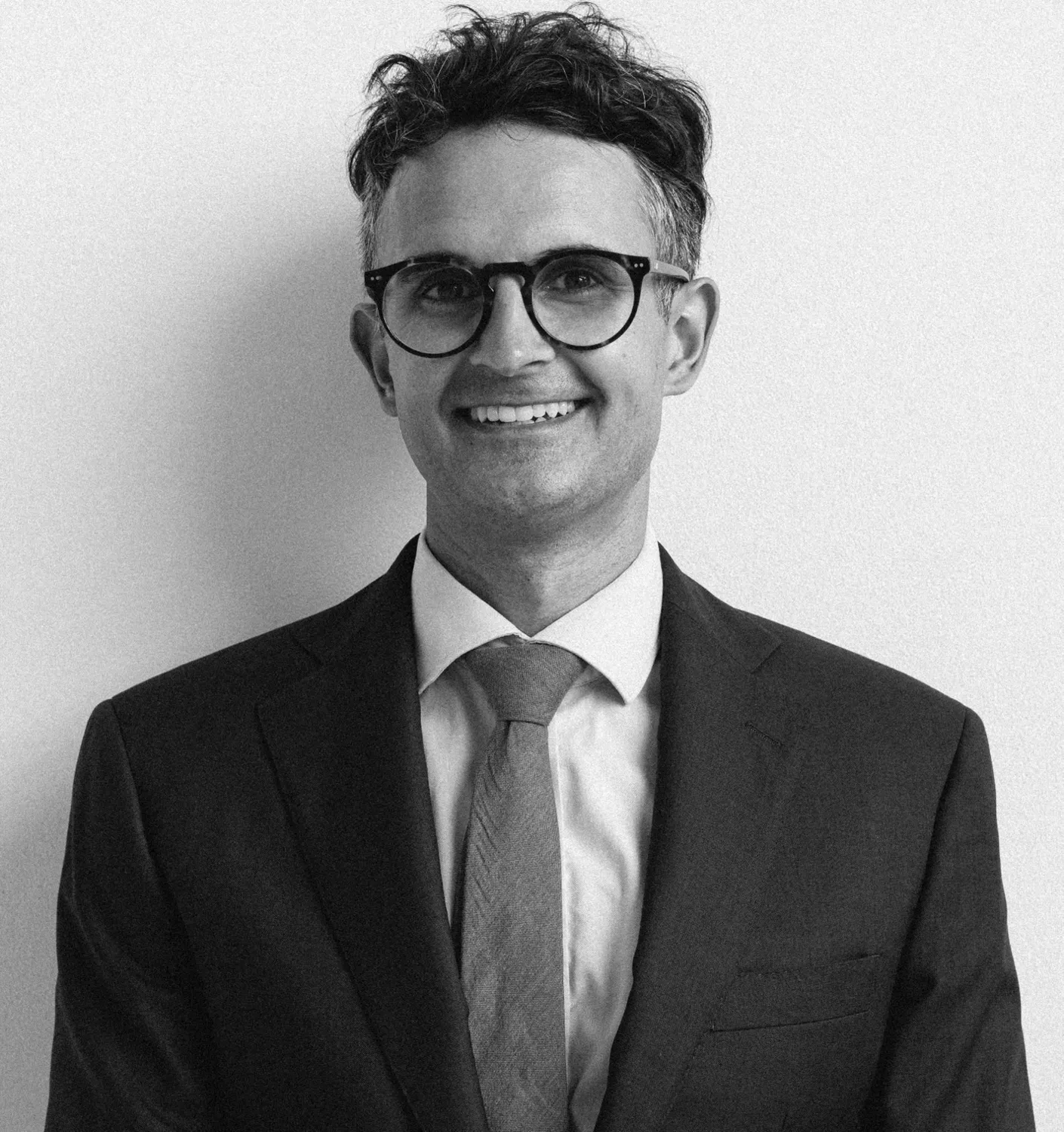 Dr Raj Narulla, orthopaedic surgeon, smiling in a dark suit and glasses