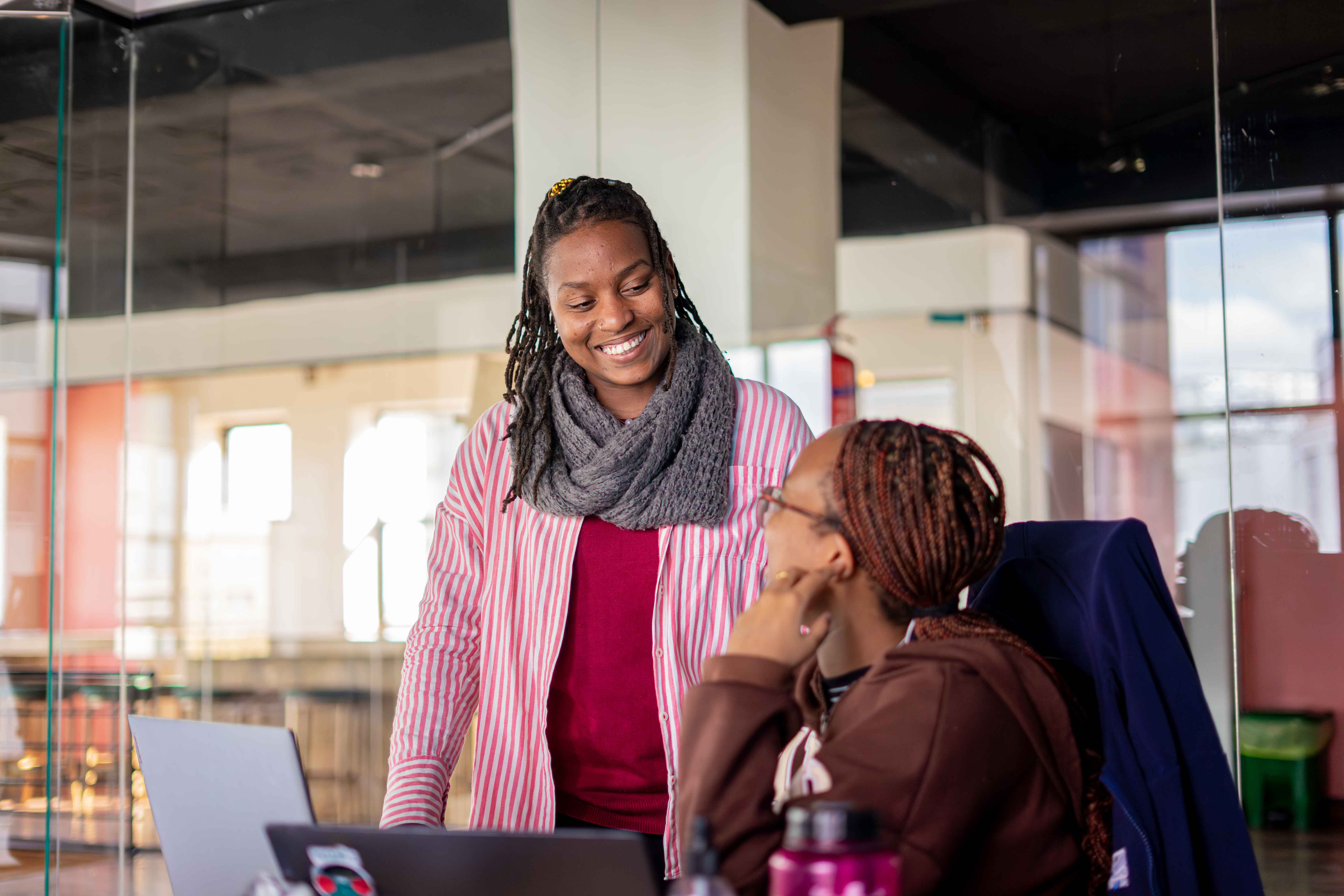 Two women in an office setting, smiling and engaging in conversation about Shamiri Academy 