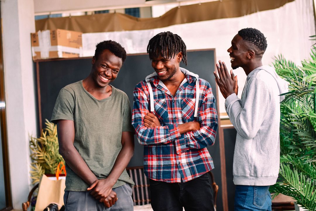 Three young men standing indoors, smiling and engaging in lively conversation Shamiri Thriving Youth