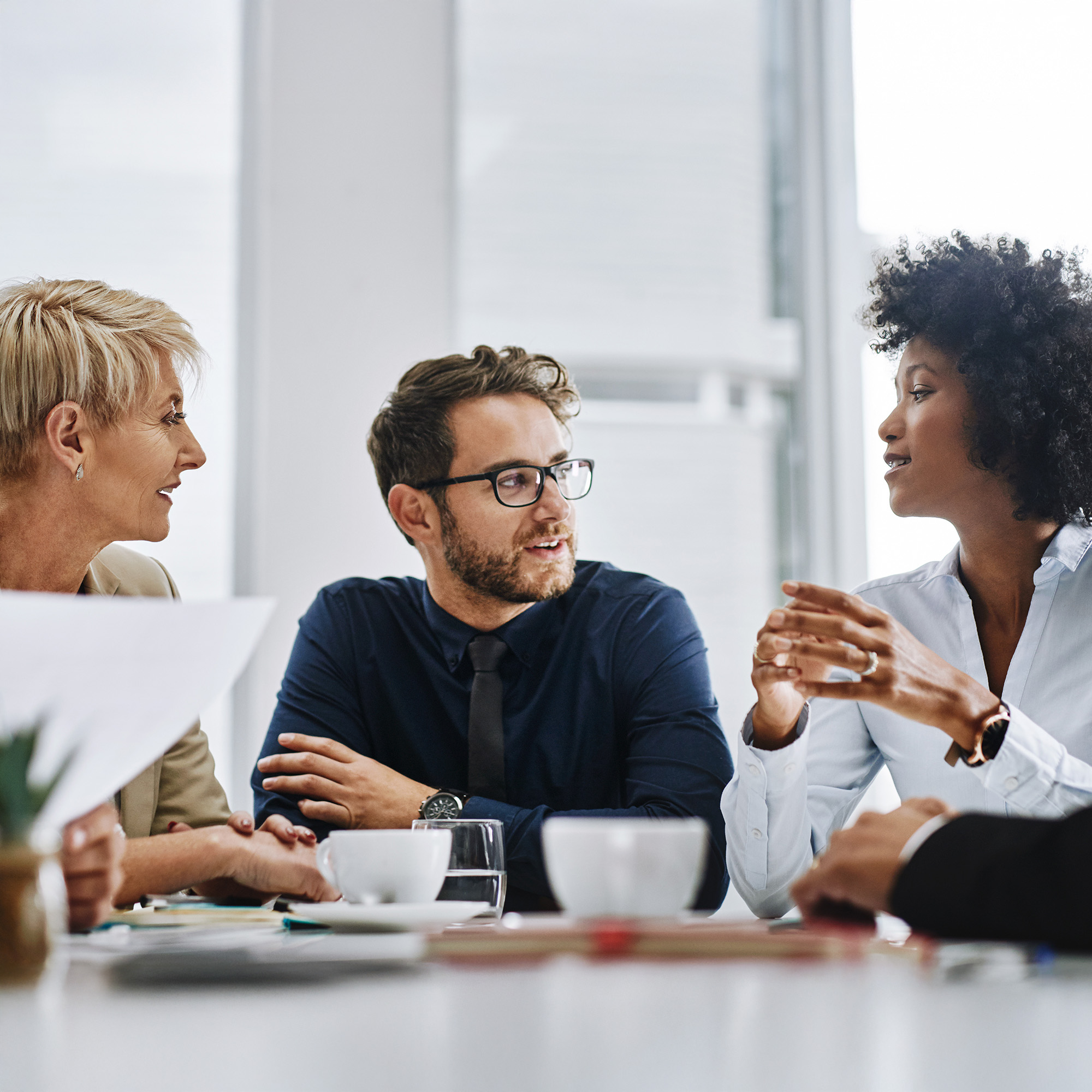 Three colleagues engaged in a discussion around a table with coffee cups and documents.