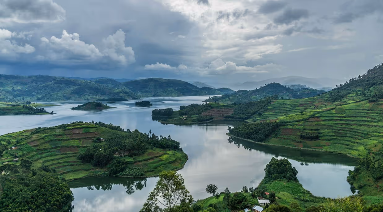 Calm lake surrounded by green terraced hills under a cloudy sky.
