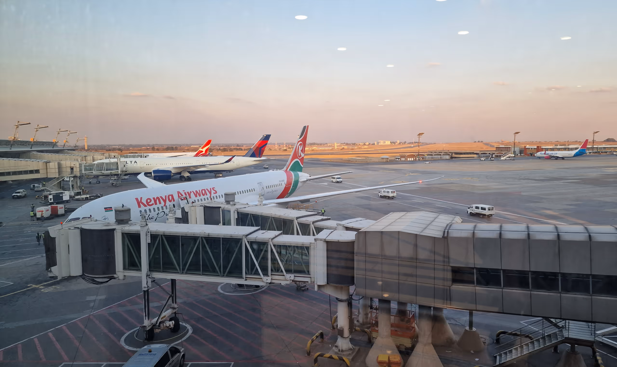 Kenya Airways plane docked at airport gate with other parked airplanes in background at sunset.