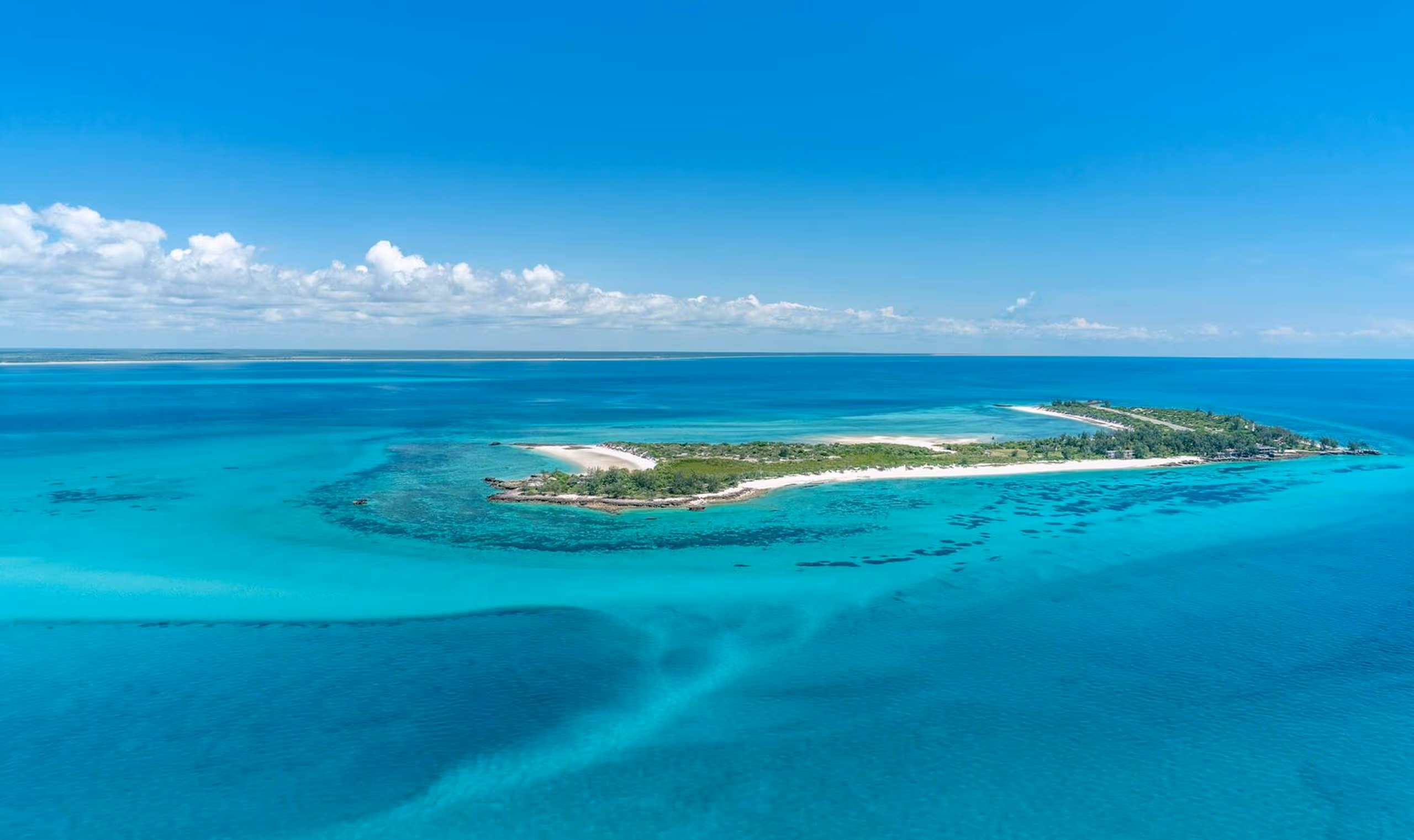 Aerial view of a tropical island surrounded by clear turquoise ocean under a bright blue sky.