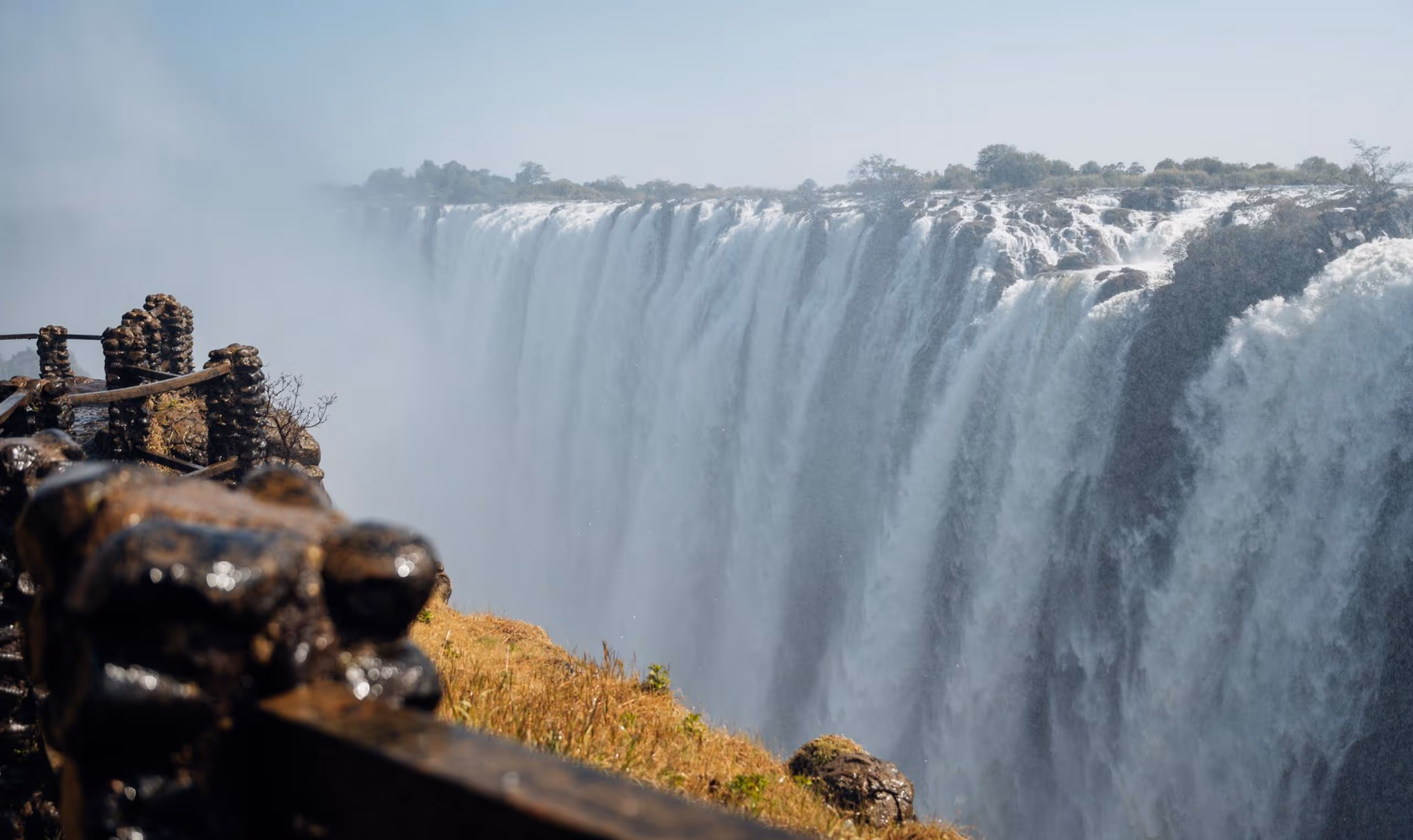 Wide view of Victoria Falls with water cascading over the edge and mist rising.