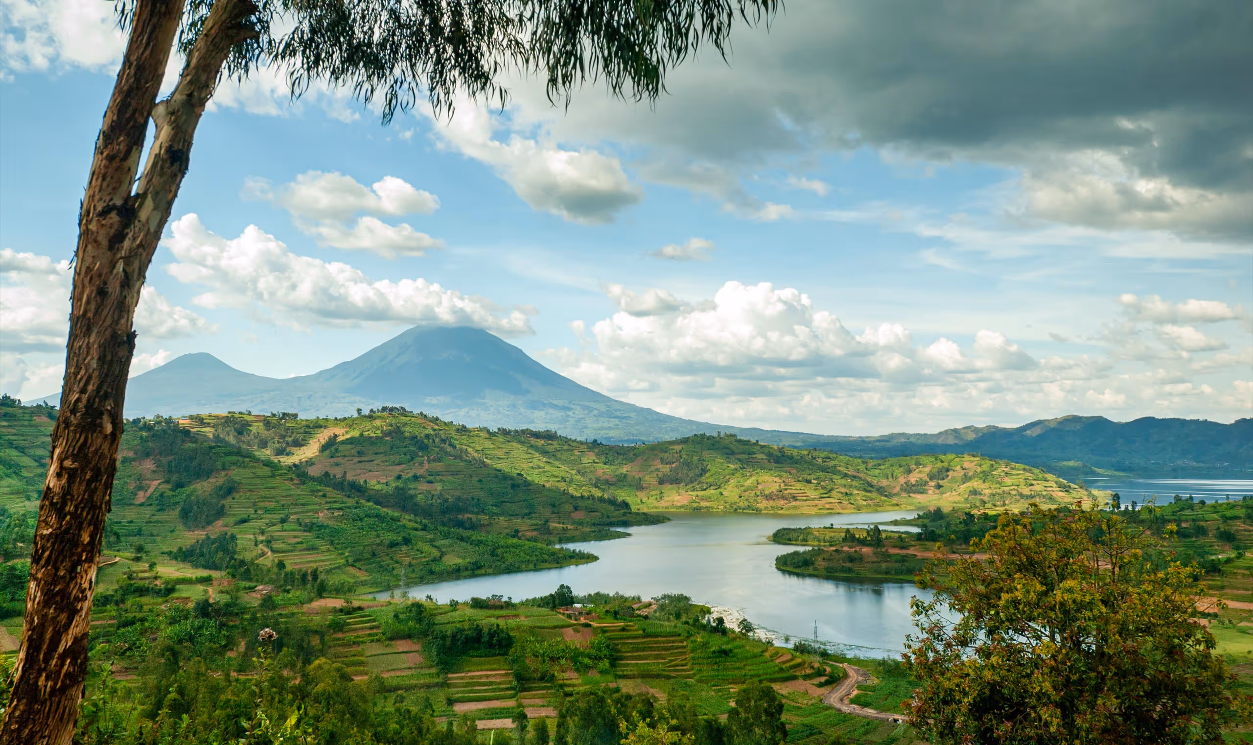 River winding through lush green hills with distant mountains under a partly cloudy sky.
