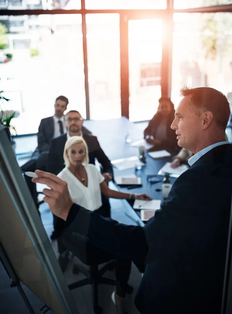 Businessman pointing at a flip chart during a meeting with attentive colleagues in a bright office.