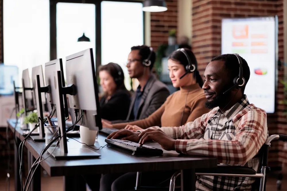 Diverse call center employees wearing headsets working on computers in an office.