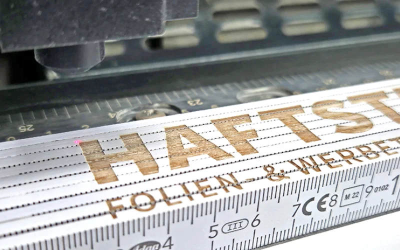 Lasergravur eines Firmenlogos auf einem Zollstock als Werbeartikel