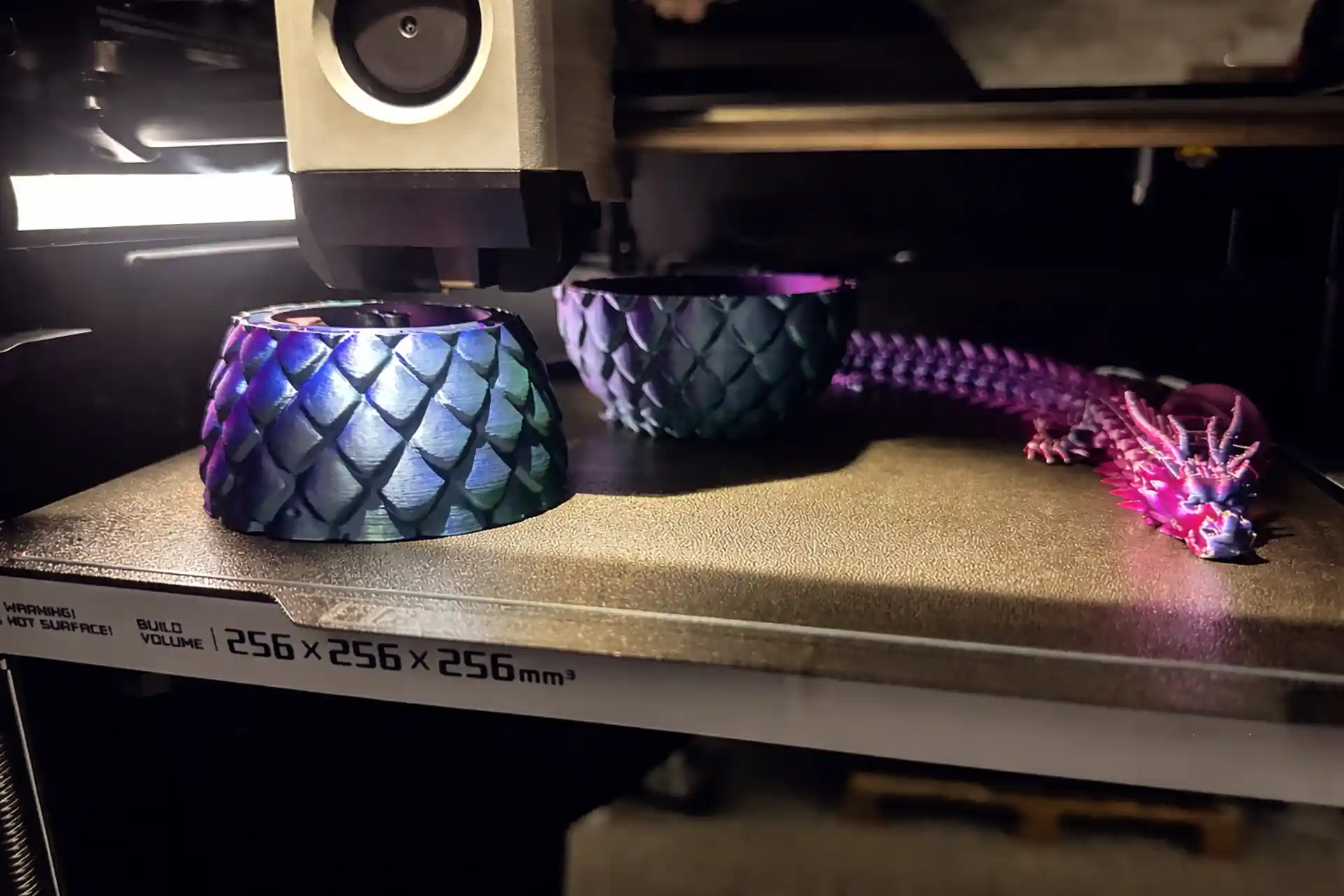 3D-Drucker fertigt detailreiche Schalen mit Schuppenmuster und einen bunten Drachen aus Kunststoff auf der Druckplatte