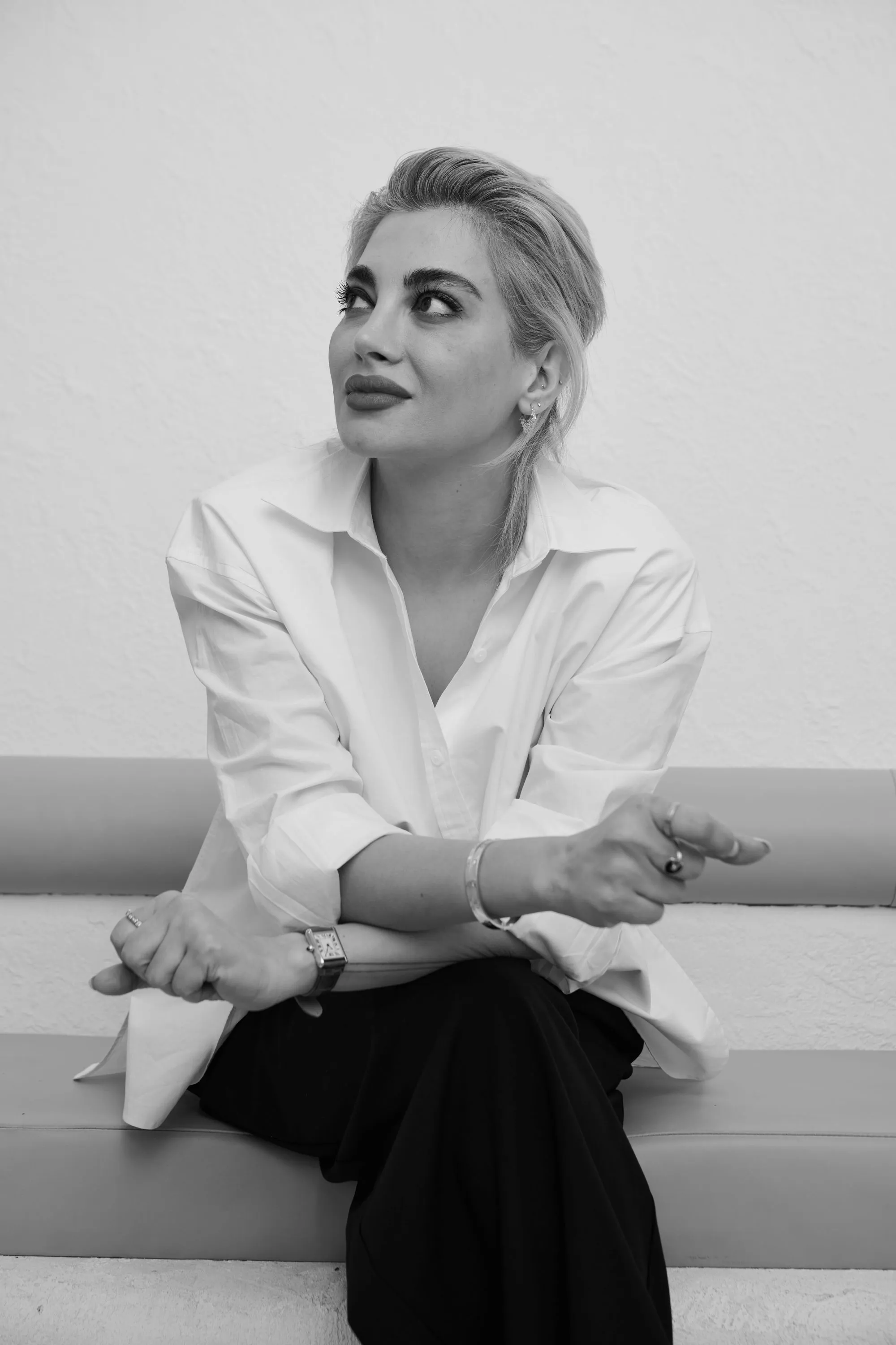 Black and white photo of a woman with short hair wearing a white shirt, sitting on a bench and looking up thoughtfully.