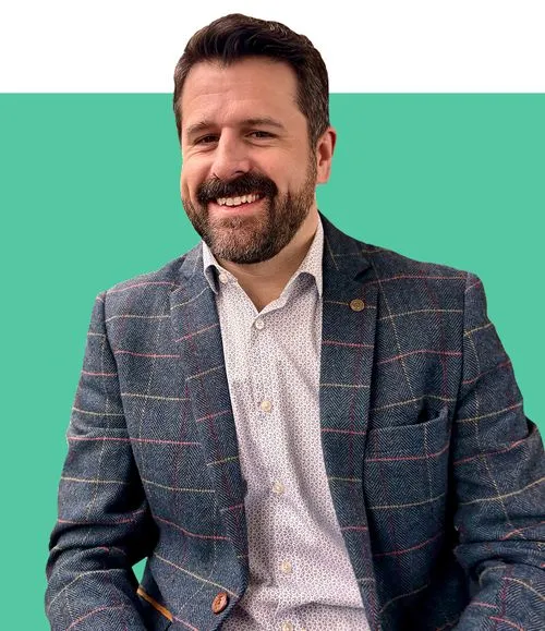 A man with a beard, shirt and checked jacket, smiling. 