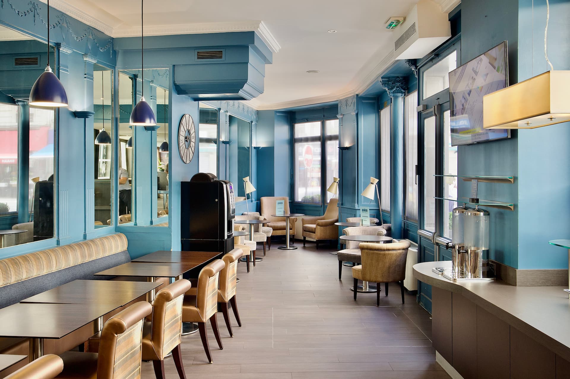 Intérieur d'un salon moderne avec murs bleu vif, tables en bois, chaises en cuir marron et fauteuils beige près des fenêtres.