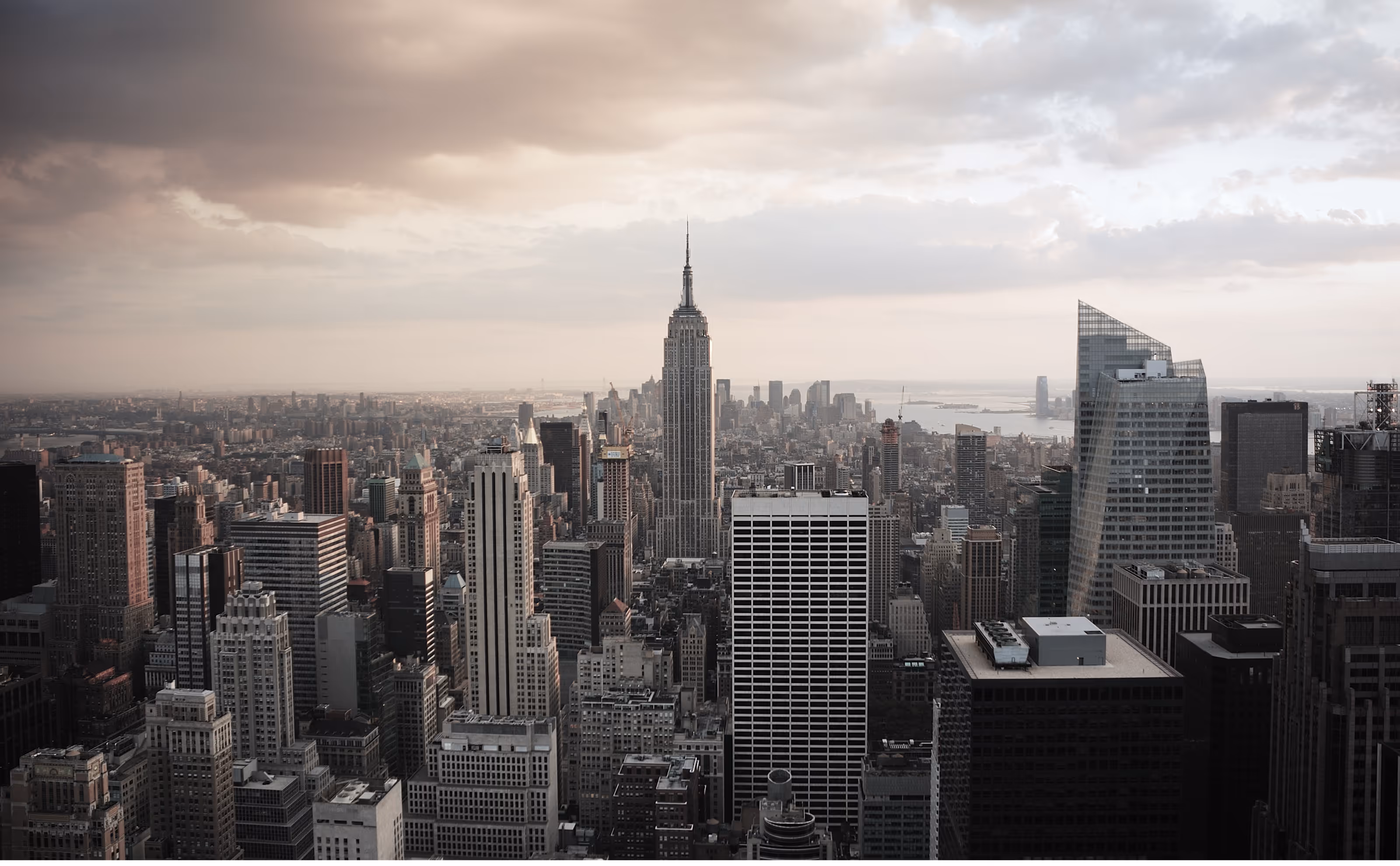 Panoramic view of New York City skyline featuring the Empire State Building under a cloudy sky.