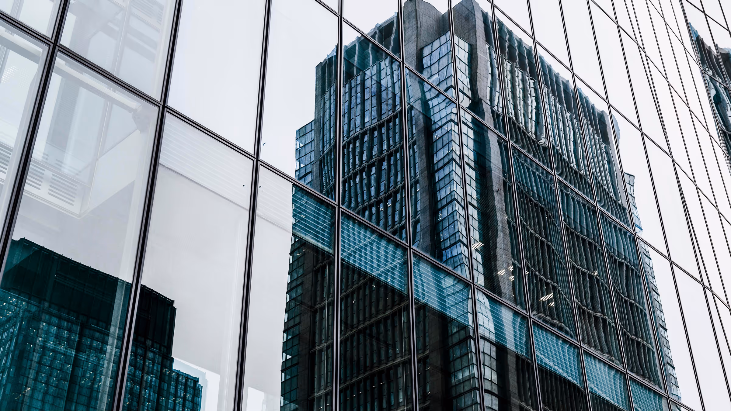 Reflection of a tall modern office building on the glass facade of another building.