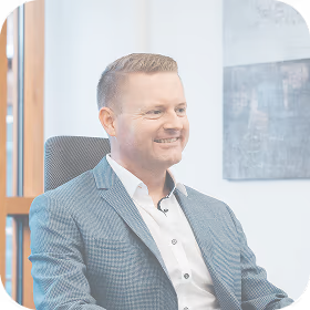 Smiling man in a blue checkered suit and white shirt sitting in an office chair.