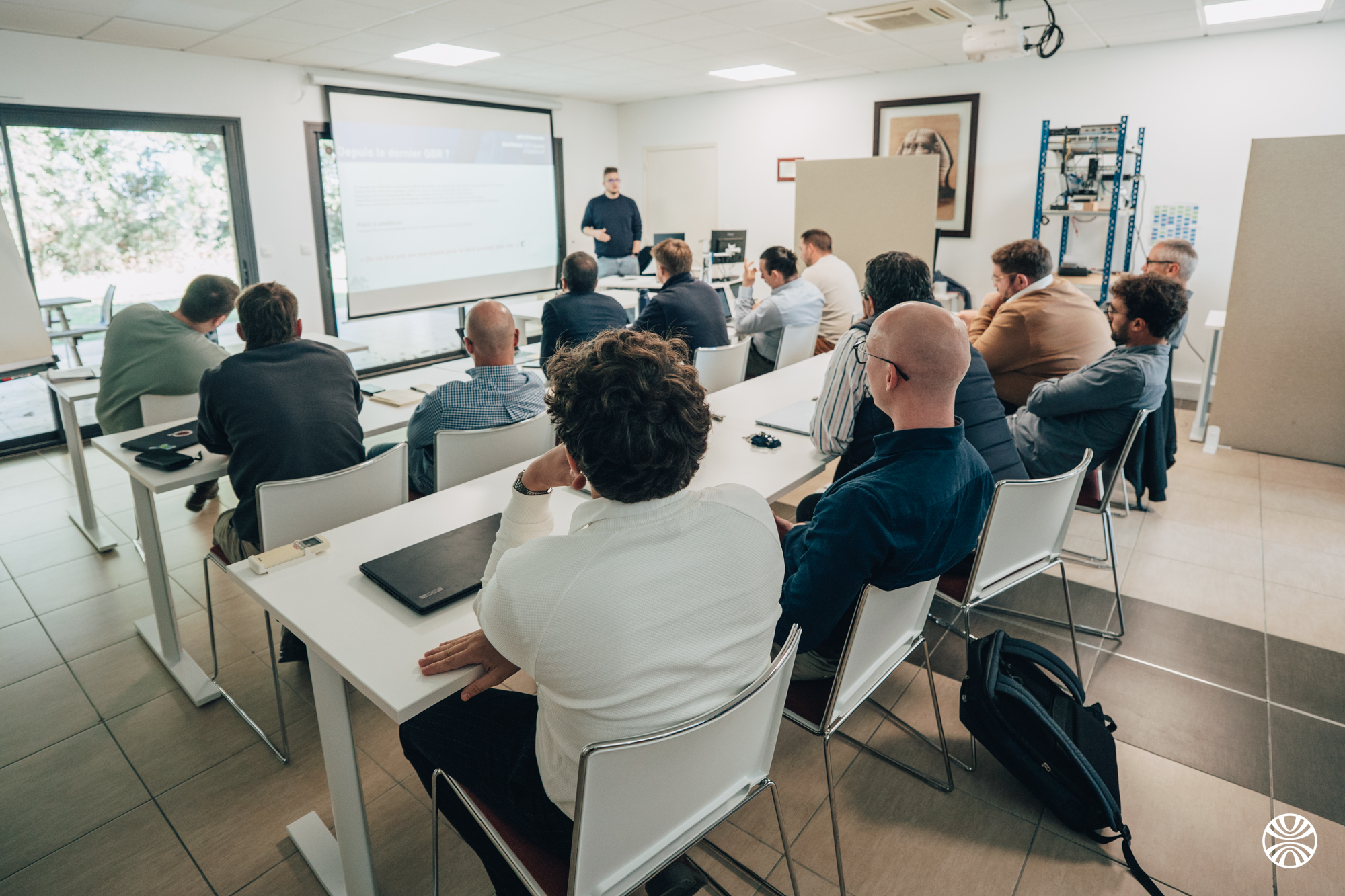 Un groupe d'adultes assis dans une salle de classe regardant une présentation projetée sur un écran.