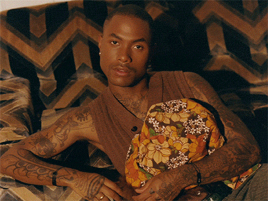 Steve Lacy reclining on patterned couch, holding a floral-patterned pillow