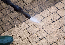 Druckwasserreiniger reinigt schmutzige Pflastersteine auf dem Boden.