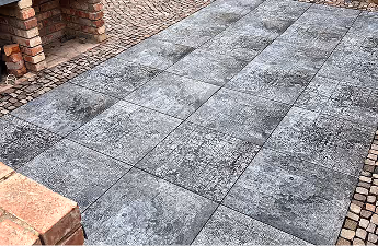 Graue Steinplatten mit strukturierter Oberfläche auf einem Gehweg neben einem Backsteinmauerwerk.