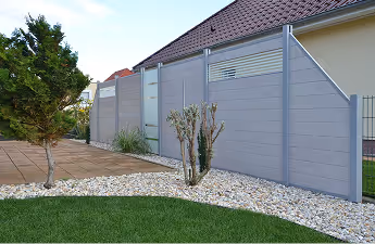 Moderner grauer Sichtschutzzaun mit Metallrahmen in einem gepflegten Garten neben einem Haus.