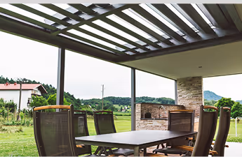 Überdachte Terrasse mit Esstisch und Stühlen vor grüner Landschaft und Bergen.