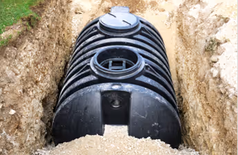 Schwarzer Kunststofftank teilweise in einem Grabenschacht vergraben mit Erdaushub ringsherum.