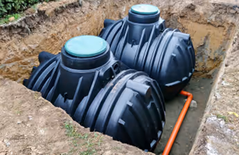 Zwei schwarz Kunststofftanks mit grünen Deckeln in einer Erdgrube mit sichtbarem orangefarbenem Rohr.