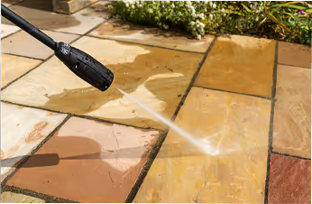 Hochdruckreiniger, der einen gepflasterten Boden aus verschiedenen farbigen Steinplatten reinigt.