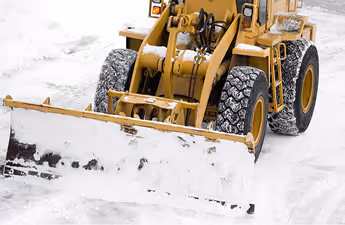 Gelber Schneepflug mit großen Reifen räumt Schnee auf einer verschneiten Straße.